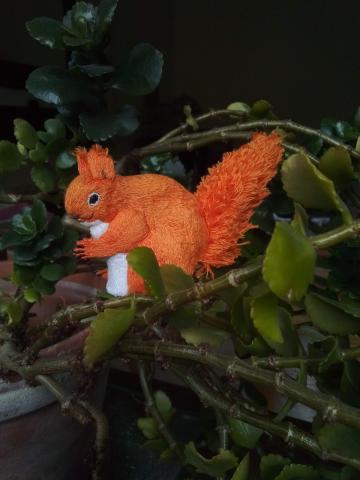 An embroidered red squirrel is sitting on one of my pot plants